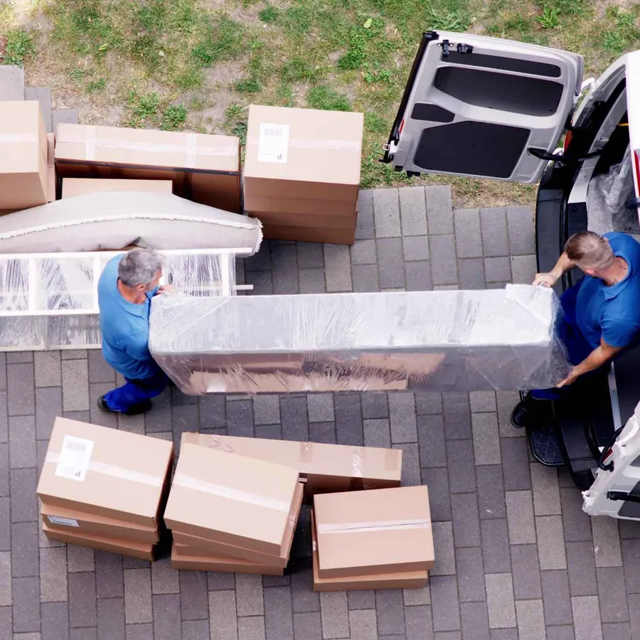 Zwei Mitarbeiter tragen ein eingepacktes Sofa zum Transporter